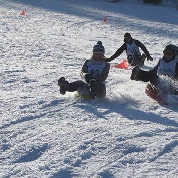 Kinder beim Rodeln im Schnee im Brandnertal in Vorarlberg während eines winterlichen Familienurlaubs.
