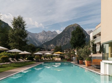 Outdoor-Pool des Hotel Valavier in Brand mit Liegewiese, Sonnenschirmen und Blick auf die Berge im Brandnertal.